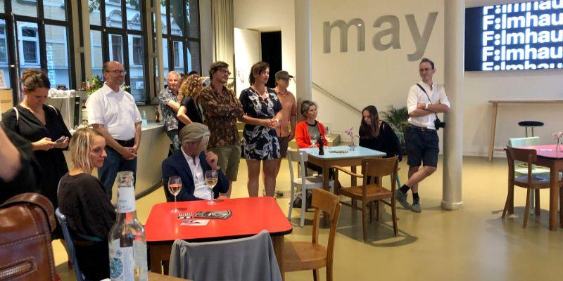 Besucher des Get-Togethes im Filmhaus Köln stehen an Tischen und hören einem Vortrag zu