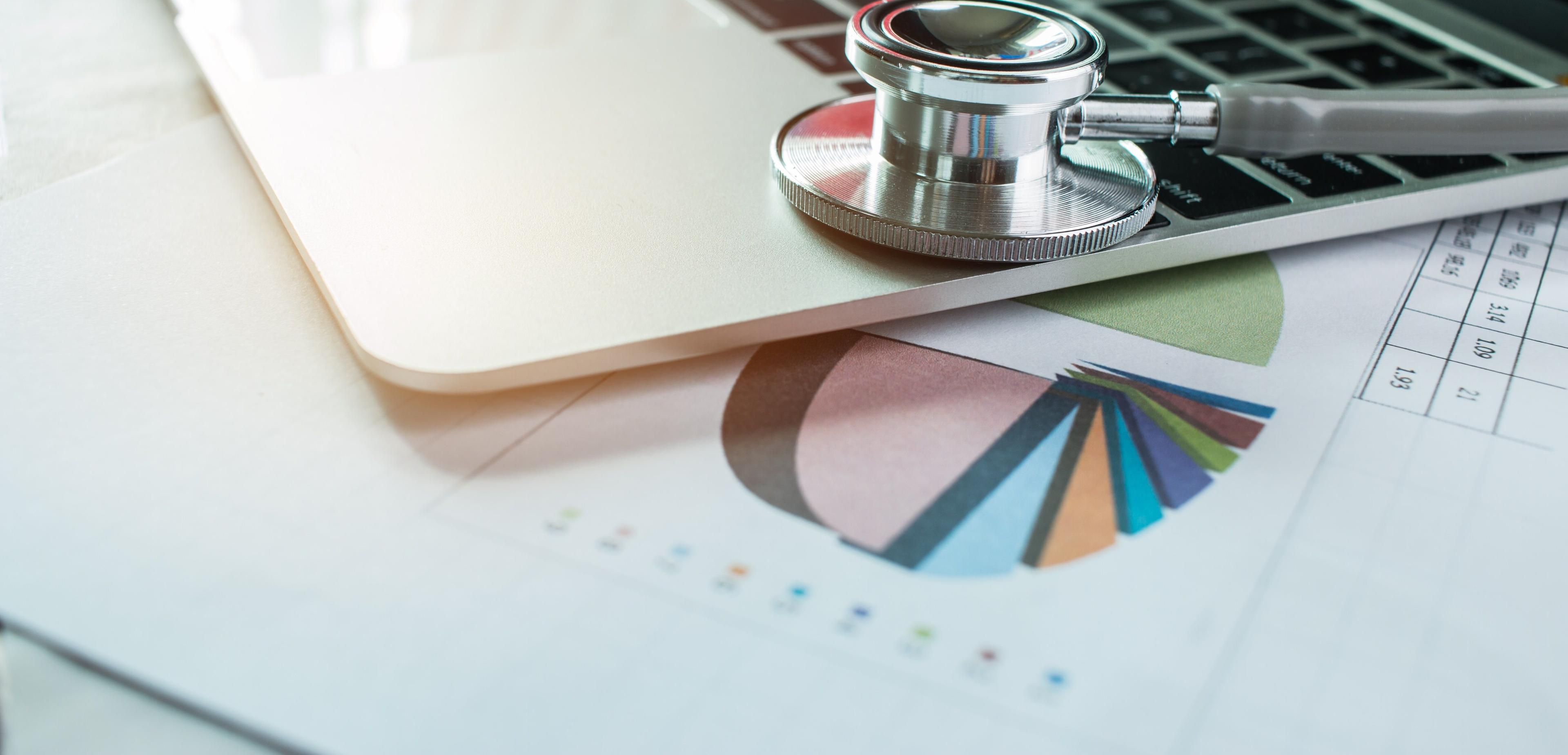 Ein Laptop liegt auf einem Ausdruck mit Statistik und Auswertungen auf dem Schreibtisch eines Verantwortliichen im Medical Controlling und Belegungsmanagement